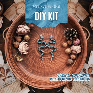 Puede incluir: Un kit de bricolaje para crear pendientes de flecos de cuentas. La imagen presenta un par de pendientes con forma de serpiente en tonos azules, blancos y negros. Los pendientes se exhiben en un plato de madera, rodeados de bellotas, flores secas y el texto "CrazyBeadKit DIY KIT". También se ve el texto "CREATE YOUR OWN BEAD FRINGE EARRINGS".