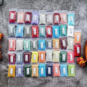 Puede incluir: Una colección de pequeñas cuentas de colores en bolsas de plástico transparente, dispuestas en filas. Las cuentas vienen en una variedad de colores, incluyendo rojo, rosa, azul, verde y amarillo. Las bolsas están selladas con cierre de cremallera. Vista superior.