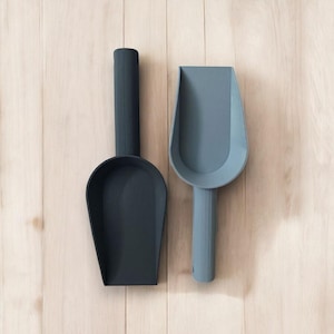 May include: Two plastic scoops, one black and one gray, hanging on a wooden wall. The scoops are designed for scooping ice cream or other loose items.