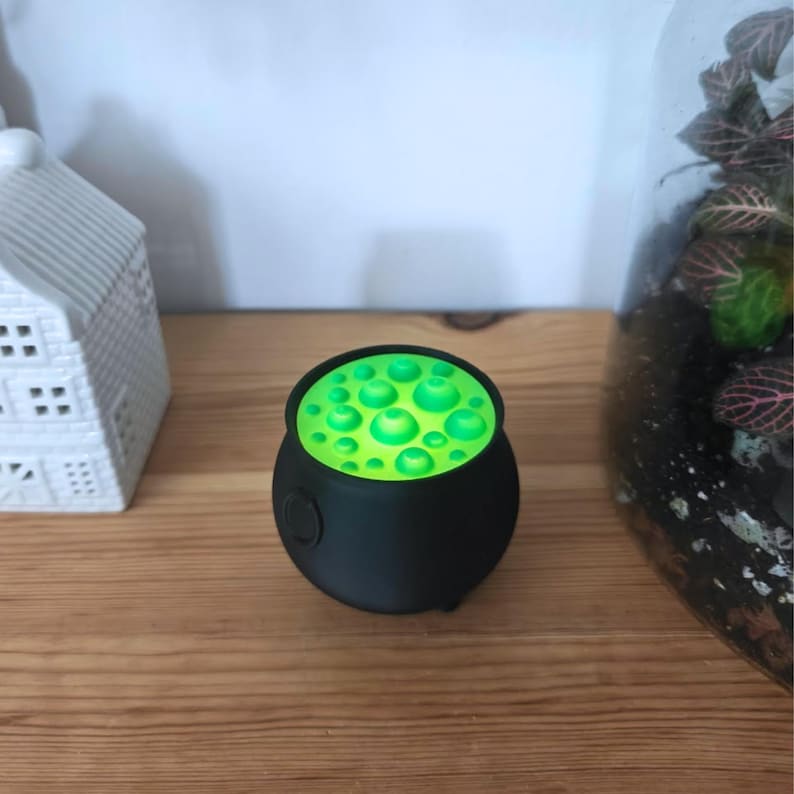 Small witch cauldron with glowing green insert, spooky Halloween shelf decoration