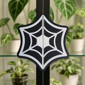 Può includere: Maniglie per ante di armadi nere e bianche con un design a ragnatela. Le maniglie hanno la forma di una stella a sei punte, con sfondo nero e dettagli a ragnatela bianchi. Le ante dell'armadio sono nere.