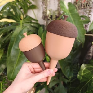 Puede incluir: Dos picos de riego para plantas con forma de bellota. El más pequeño tiene una base marrón oscuro y una tapa texturizada color canela. El más grande tiene una base color canela y una tapa texturizada marrón oscuro, con un tallo puntiagudo.