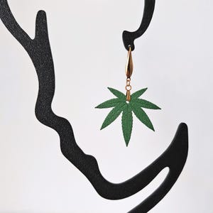 Op de afbeelding: Een groene marihuana-blad hangende oorbel met een gouden ketting en haak.