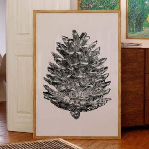Op de afbeelding: Een groot ingelijste kunstdruk met een gedetailleerde zwart-wit illustratie van een dennenappel. Het kunstwerk wordt getoond in een kamer met houten vloeren en een neutraal kleurenpalet, wat een moderne esthetiek creëert.