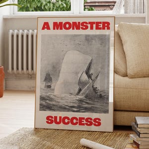 May include: A framed poster with a black and white illustration of a whale attacking a ship. The poster has the text "A MONSTER" at the top and "SUCCESS" at the bottom, both in red.