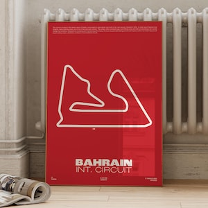 Puede incluir: Un póster enmarcado con fondo rojo presenta un contorno blanco del circuito internacional de Bahréin. El texto "BAHRAIN INT. CIRCUIT" se muestra en blanco en la parte inferior. El póster está apoyado contra una pared.