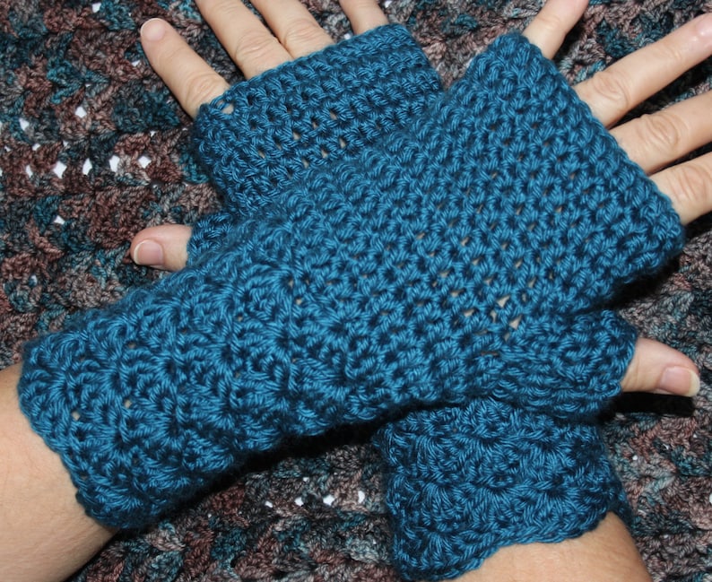 May include: A pair of teal blue crocheted fingerless gloves. The gloves are made with a simple stitch pattern and have a loose fit.