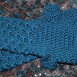May include: A pair of teal blue crocheted fingerless gloves. The gloves are made with a textured stitch and have a scalloped edge.