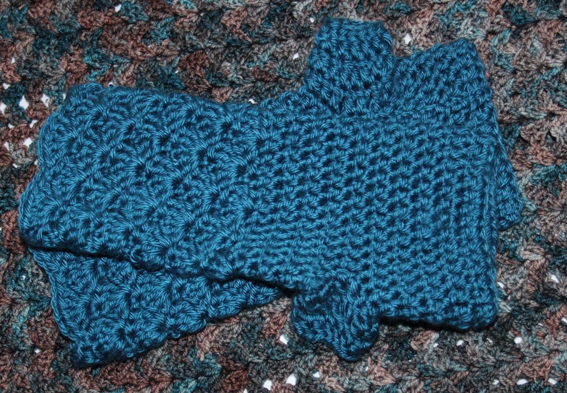May include: A pair of teal blue crocheted fingerless gloves. The gloves are made with a textured stitch and have a scalloped edge.