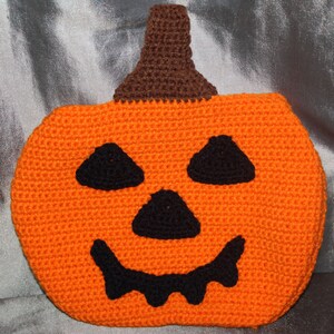 May include: Orange crocheted pumpkin with a black smiling face. The pumpkin has a brown crocheted stem.
