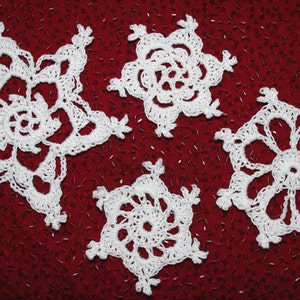 May include: Five white crocheted snowflakes on a red background. The snowflakes are all different designs and have a delicate, lacy appearance.