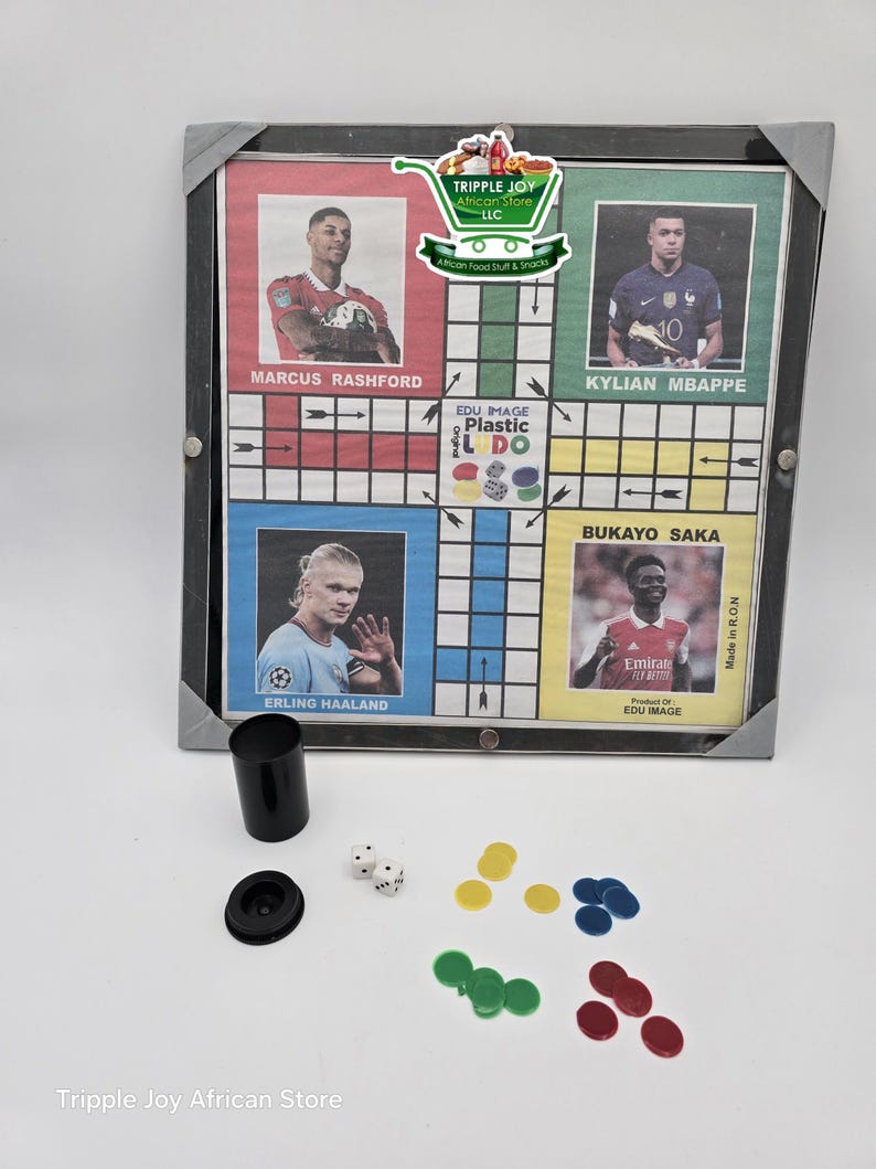 May include: A plastic Ludo board game with a black frame. The board features images of famous soccer players, including Marcus Rashford, Kylian Mbapp&eacute;, Bukayo Saka, and Erling Haaland. The game includes four colored playing pieces, two dice, and a cup.