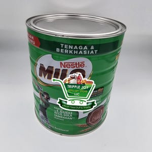 May include: A green and silver Milo tin with the Nestle logo. The tin has text in multiple languages, including "TENAGA & BERKHASIAT" and "Malt Coklat Berkhasiat". A sticker for "TRIPPLE JOY African Store" is on the front.