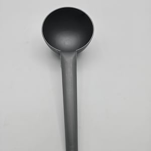 May include: A gray plastic scoop with a long handle and a rounded bowl. The scoop is designed for measuring and dispensing dry ingredients. The handle has a hole at the end for hanging. The text "Tripple Joy African Store" is at the bottom.