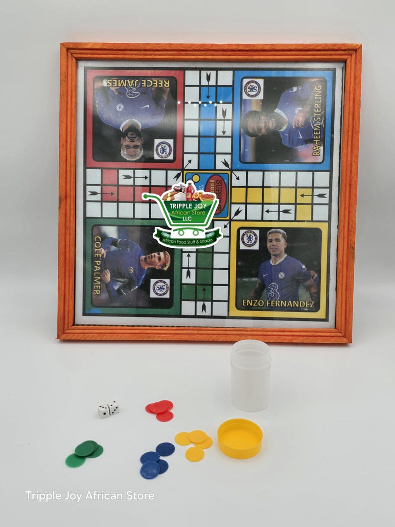 May include: A wooden framed game board with a colorful checkerboard pattern. The board features images of soccer players and the text "Cole Palmer", "Reece James", "Raheem Sterling", and "Enzo Fernandez". The game board is accompanied by a white plastic container, two white dice, and a set of colorful game pieces.