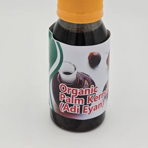 May include: A small glass bottle with a yellow lid filled with a dark liquid. The label reads "Organic Palm Kernel (Adi Eyan)".