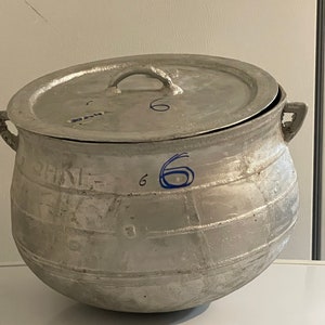 May include: A large, silver, aluminum pot with a lid. The pot has a rounded bottom and a wide opening. The lid has a handle and is slightly ajar. The pot is marked with the number "6" on the side.