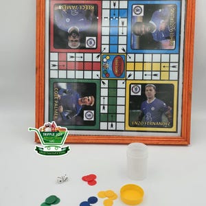 May include: A wooden framed board game with a colorful grid and images of soccer players. The game is called "Supreme Ludo Game". There are also dice, counters, and a container for the counters.