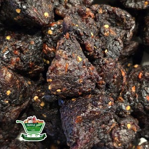 May include: Close-up of a pile of dark brown, textured food items with visible red pepper flakes. The food appears to be a snack or a type of jerky. The image is from the Tripple Joy African Store.