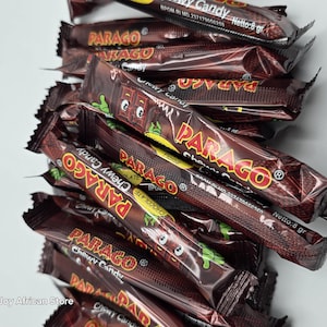 May include: A pile of individually wrapped chocolate chewy candy bars with the brand name "PARAGO" printed on the wrappers. The wrappers are brown and have a gold and red design. The candy bars are 8 grams each.