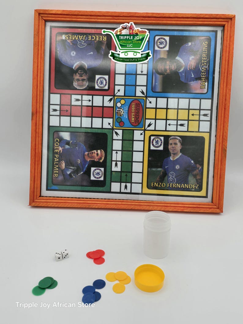 May include: A wooden framed game board with a colorful design and images of soccer players. The board is surrounded by a set of colorful game pieces, two dice, and a white container.