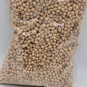 May include: A clear plastic bag filled with light brown soybeans. The soybeans are tightly packed, filling the bag. The text "Tripple Joy African Store" is visible at the bottom of the bag.