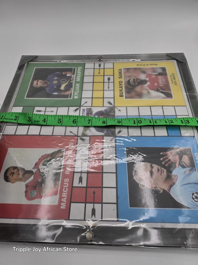 May include: A game board with a grid of squares and arrows. The board features photos of soccer players, including Kylian Mbappe, Bukayo Saka, Marcus Rashford, and Erling Haaland. The board is made of cardboard and is covered in plastic.