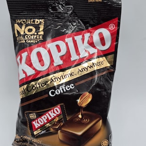 May include: A black bag of Kopiko coffee-flavored hard candy. The bag has red and gold accents with the words "Kopiko" and "Real Coffee Anytime, Anywhere." A smaller image of the candy is on the front.