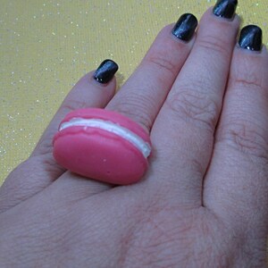 May include: A pink and white macaron-shaped ring. The ring is made of a soft, pliable material and is designed to look like a real macaron.