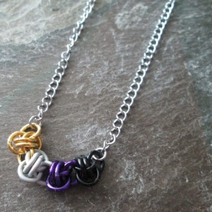 May include: A silver chain necklace with a series of linked knots in gold, silver, purple, and black.