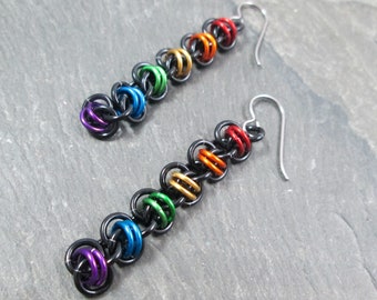 May include: A pair of rainbow colored earrings with black metal rings and silver hooks. The earrings are made with small, linked rings in a rainbow pattern.