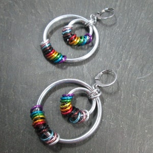 May include: A pair of silver hoop earrings with rainbow colored rings. The earrings have a simple hook closure.