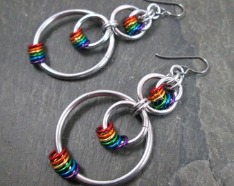 May include: A pair of silver earrings with rainbow colored rings. The earrings are made of multiple interlocking circles.