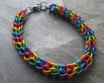 May include: A rainbow colored chainmail bracelet with a silver clasp. The bracelet is made of small metal rings that are linked together in a pattern.