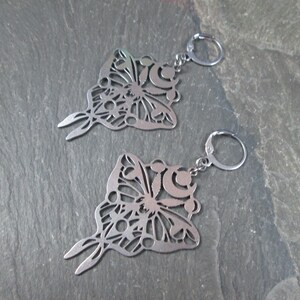 May include: A pair of silver butterfly earrings with intricate cutouts. The earrings are made of stainless steel and have a delicate, feminine design.
