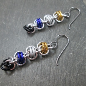 May include: A pair of silver earrings with blue and gold beads. The earrings are made of metal and have a simple design.