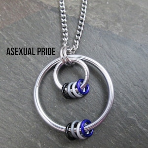 May include: A silver chain necklace with a pendant featuring two interlocking circles and a cluster of small rings in black, gray, white, and blue. The pendant is a symbol of asexual pride.