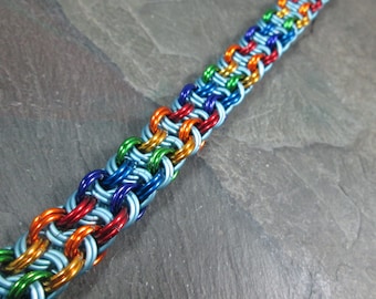 May include: A rainbow colored chainmail bracelet made of metal rings. The bracelet is made with alternating colors of silver, red, orange, yellow, green, blue, and purple.