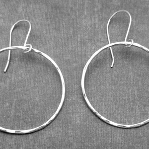 May include: A pair of silver hoop earrings with a hammered texture. The earrings are circular and have a simple design.