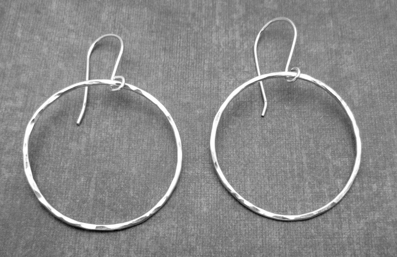May include: A pair of silver hoop earrings with a hammered texture. The earrings are circular and have a simple design.