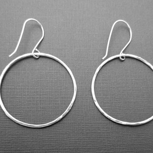 May include: A pair of silver hoop earrings with a hammered texture. The hoops are circular and have a simple design.