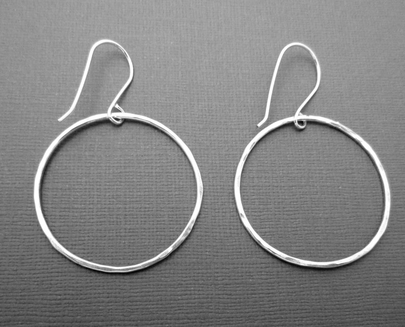 May include: A pair of silver hoop earrings with a hammered texture. The hoops are circular and have a simple design.