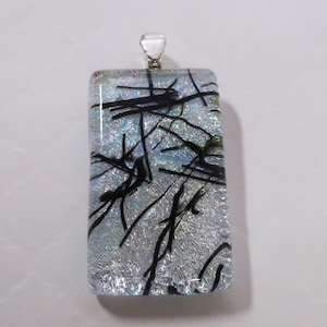 May include: Rectangular dichroic glass pendant with a silver bail. The pendant features a shimmering, iridescent background with black linear accents. The glass has a textured appearance, creating a unique visual effect. A stylish accessory.