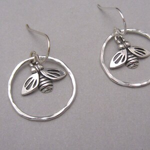 May include: Silver earrings with a hammered circle design and a small bee charm hanging from each earring.