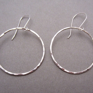 May include: A pair of silver hoop earrings with a hammered texture. The hoops are about 2 inches in diameter.