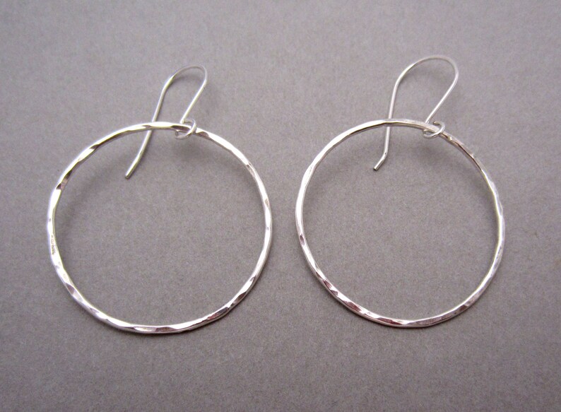 May include: A pair of silver hoop earrings with a hammered texture. The hoops are about 2 inches in diameter.
