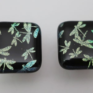 May include: Two square glass tiles with a black background and a pattern of iridescent green dragonflies.