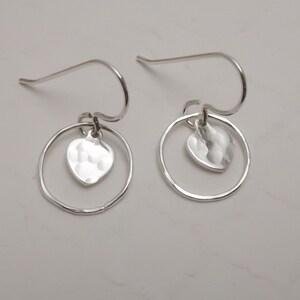 May include: A pair of silver dangle earrings with a hammered heart charm hanging from a circle.