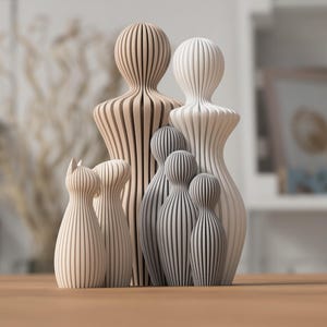 Könnte beinhalten: Eine Sammlung von Holzfiguren in verschiedenen Größen und Formen, darunter menschenähnliche Formen und eine katzenförmige Figur. Die Figuren sind hellbraun und grau, mit vertikalen Streifen. Sie sind auf einer Holzoberfläche angeordnet.