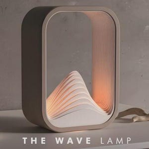 Könnte beinhalten: Moderne, rechteckige Tischlampe mit wellenförmigem Design. Die Lampe hat einen beigefarbenen Rahmen, einen weißen und orangefarbenen Innenraum und den Text "THE WAVE LAMP" unten. Die Lampe ist für eine Umgebungsbeleuchtung konzipiert, ca. 25 cm hoch.